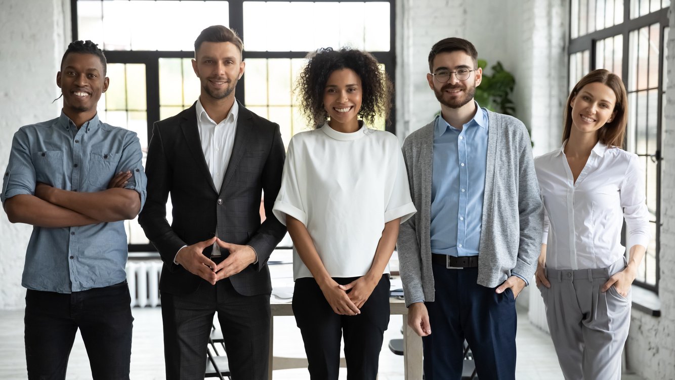 Standing in row smiling diverse team posing differently.